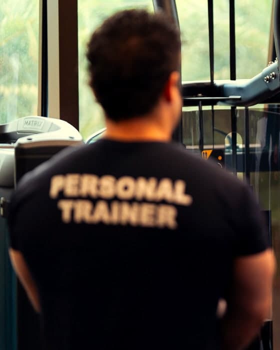 Theus de costas, com a camiseta escrita Personal Trainer, orientando na academia